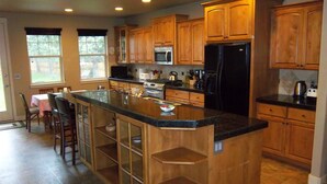 A spacious kitchen with wooden cabinets, a central island, and a dining area with chairs and a table. - Skyline Lodge, Gorgeous Setting, Walk to Downtown! (Bend)