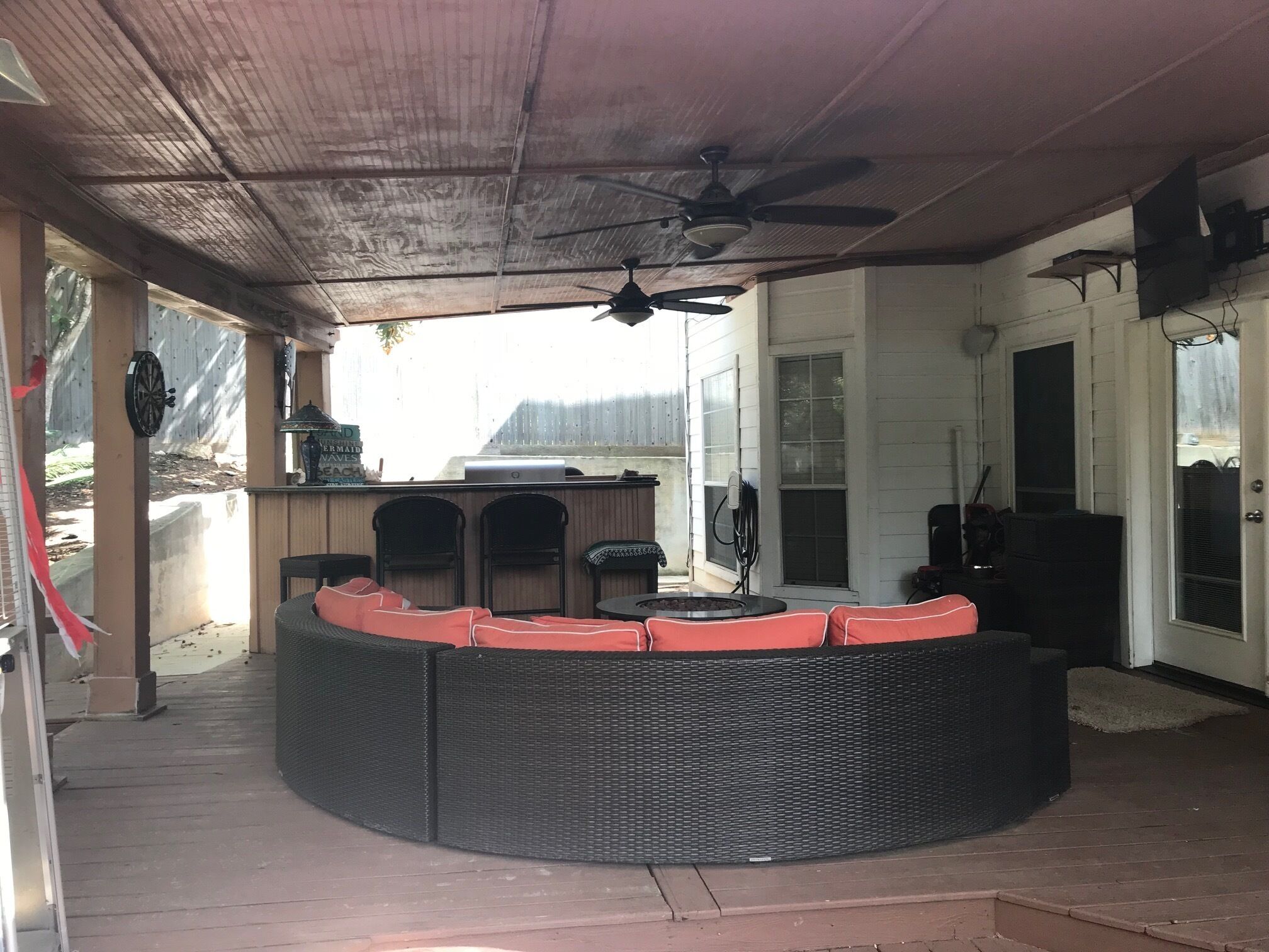 An outdoor covered patio area with a curved seating arrangement, a ceiling fan, and a view of the backyard.