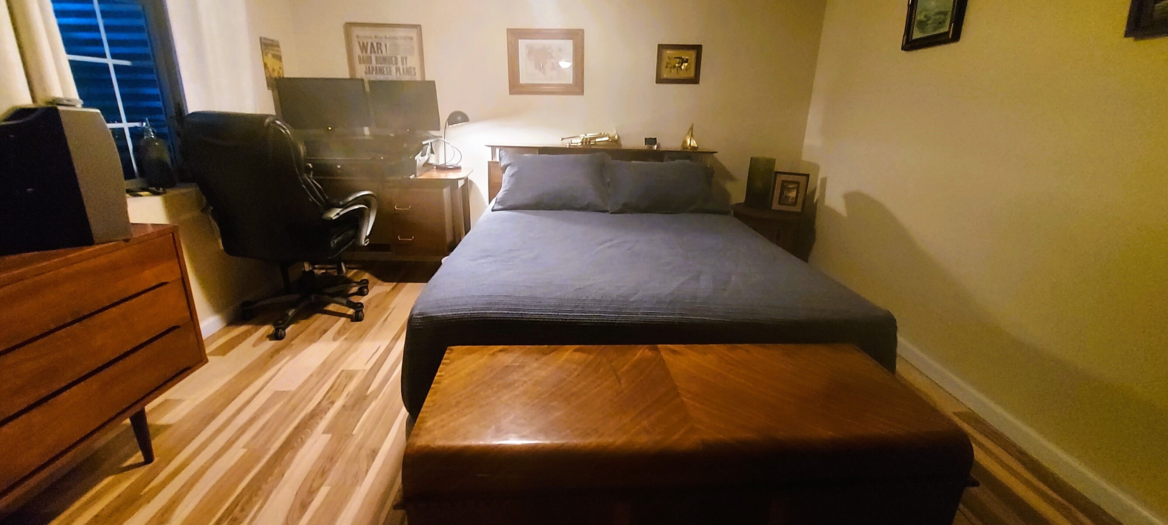 A bedroom with a bed, a wooden bench, a desk with a chair, a television, and a window with blinds.