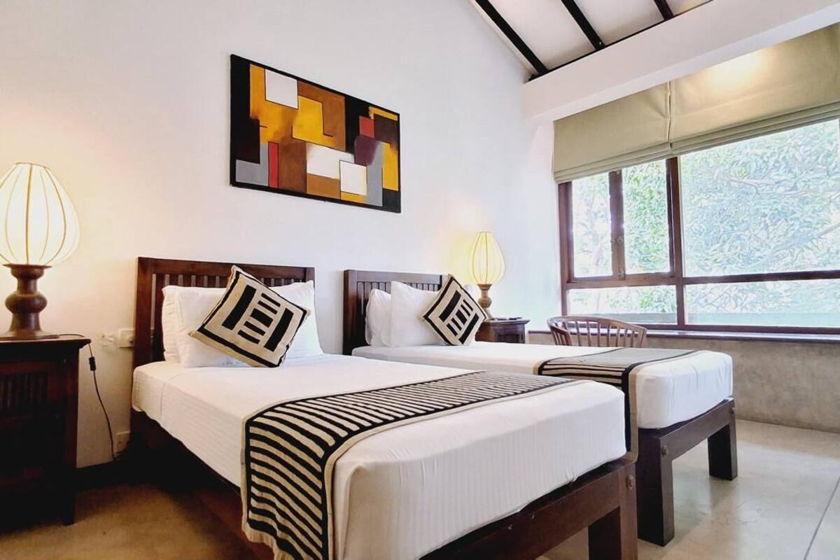 A hotel room with two beds, a large window, and a geometric artwork on the wall.