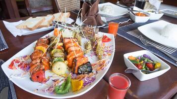 Una mesa de comedor con una fuente de brochetas a la parrilla, un tazón de ensalada y un vaso de jugo.