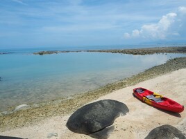 Un kayak en una playa arenosa con aguas claras y rocas al fondo.