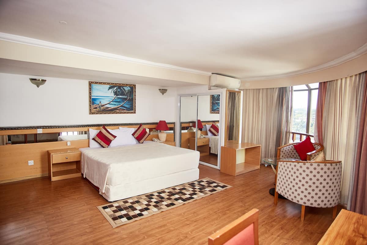 A hotel room with a large bed, a small desk, a chair, a mirror, and a view of the outdoors.