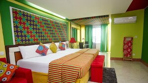 Una camera d'albergo con un letto grande, un divano rosso, un tappezzeria colorata e una tenda verde.