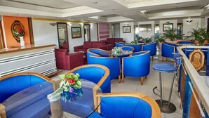 Una hall d'albergo con sedute blu e rosse, una reception e una parete decorativa.