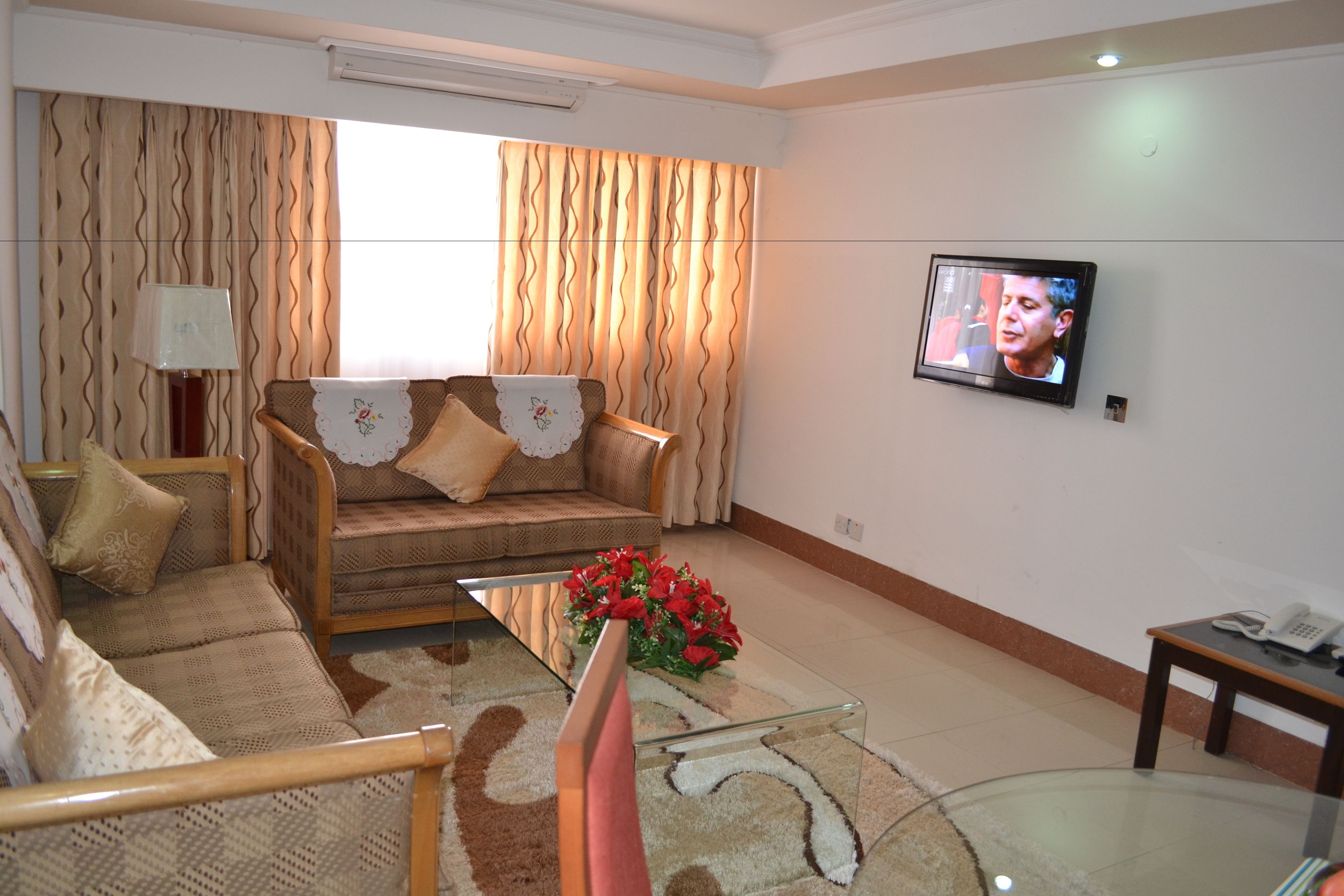 A living room with a sofa, a glass coffee table with flowers, a television, and a small table with a phone.