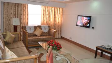 A living room with a sofa, a glass coffee table with flowers, a television, and a small table with a phone.