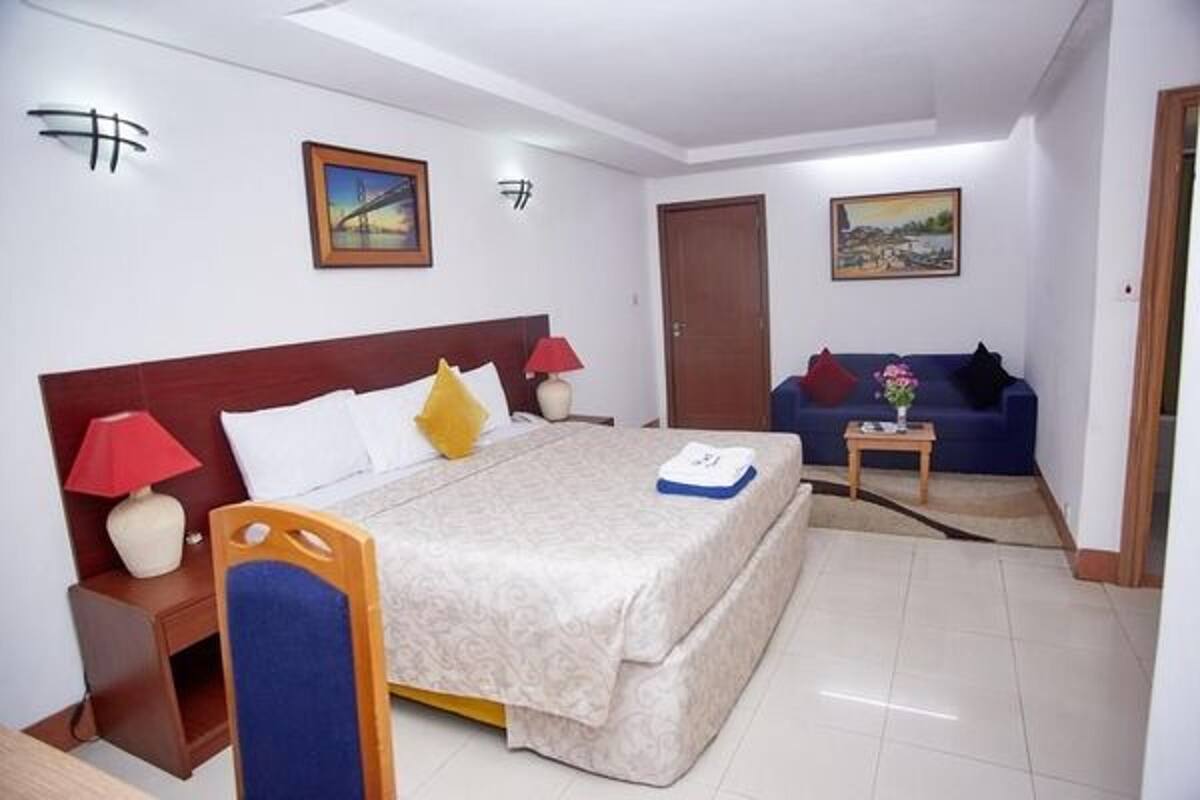A hotel room with a bed, a sofa, a nightstand, and a painting on the wall.