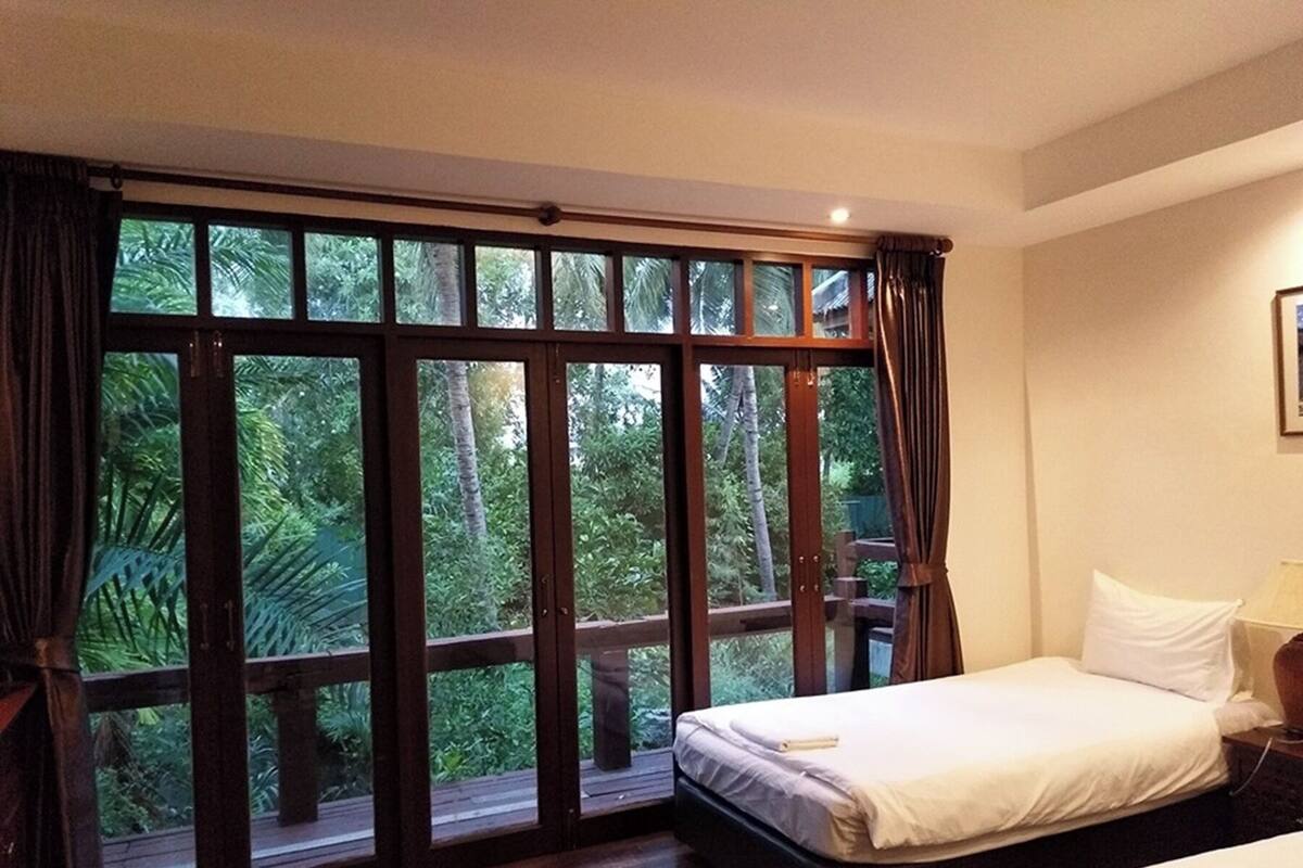 A bedroom with a large window offering a view of lush greenery.