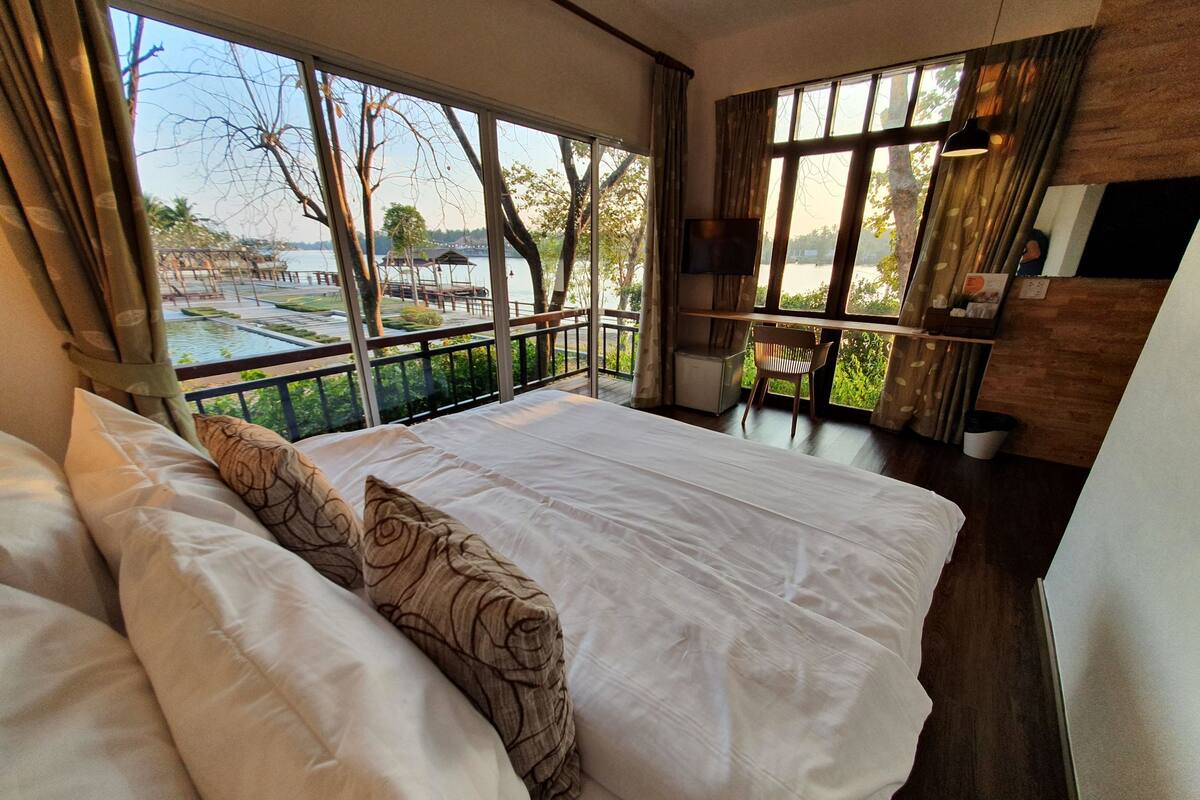 A bedroom with a large bed, a view of a lake, and a balcony with a table and chair.