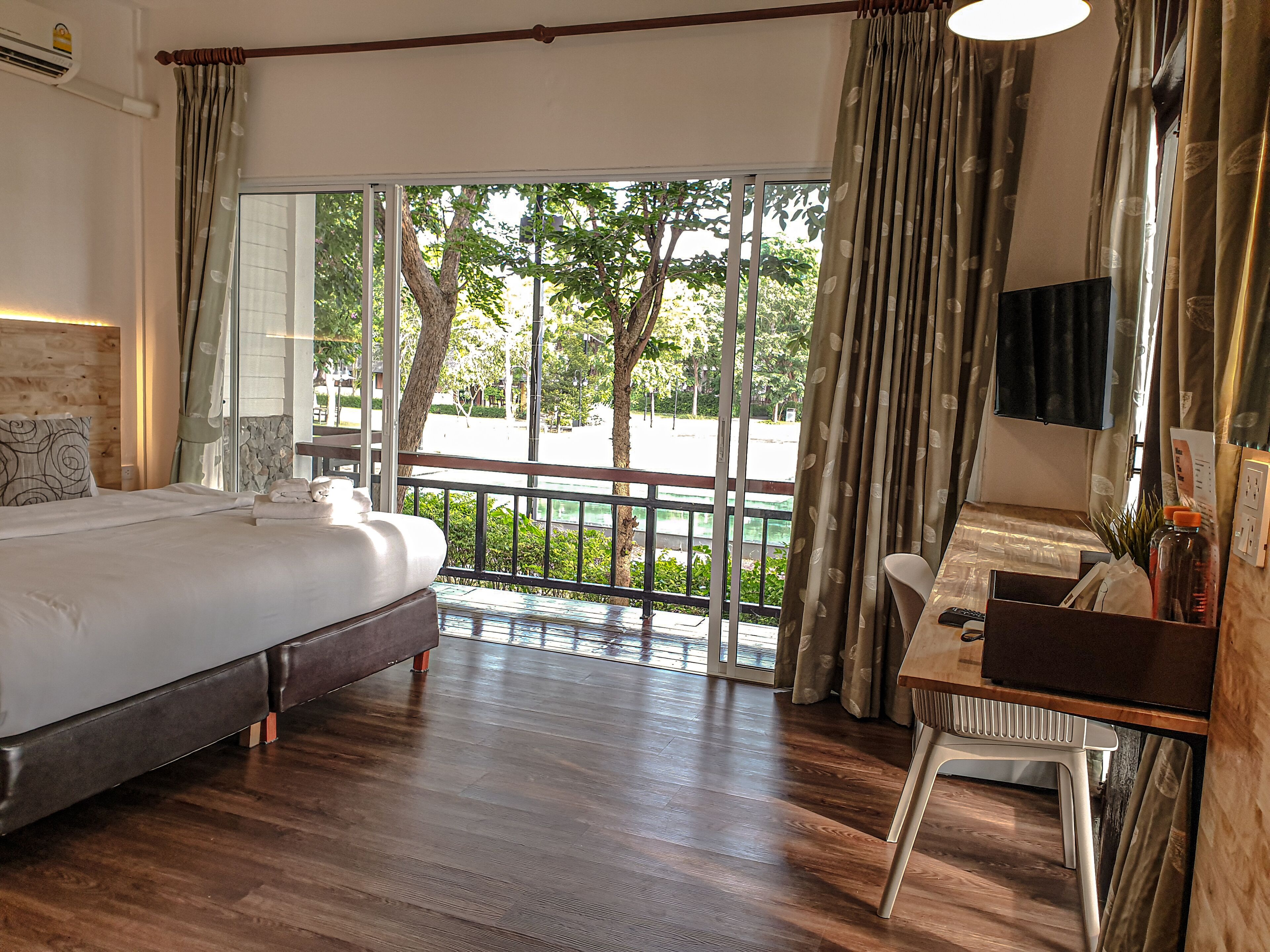 Une chambre d’hôtel avec un lit, un bureau et une vue sur un balcon bordé d’arbres.