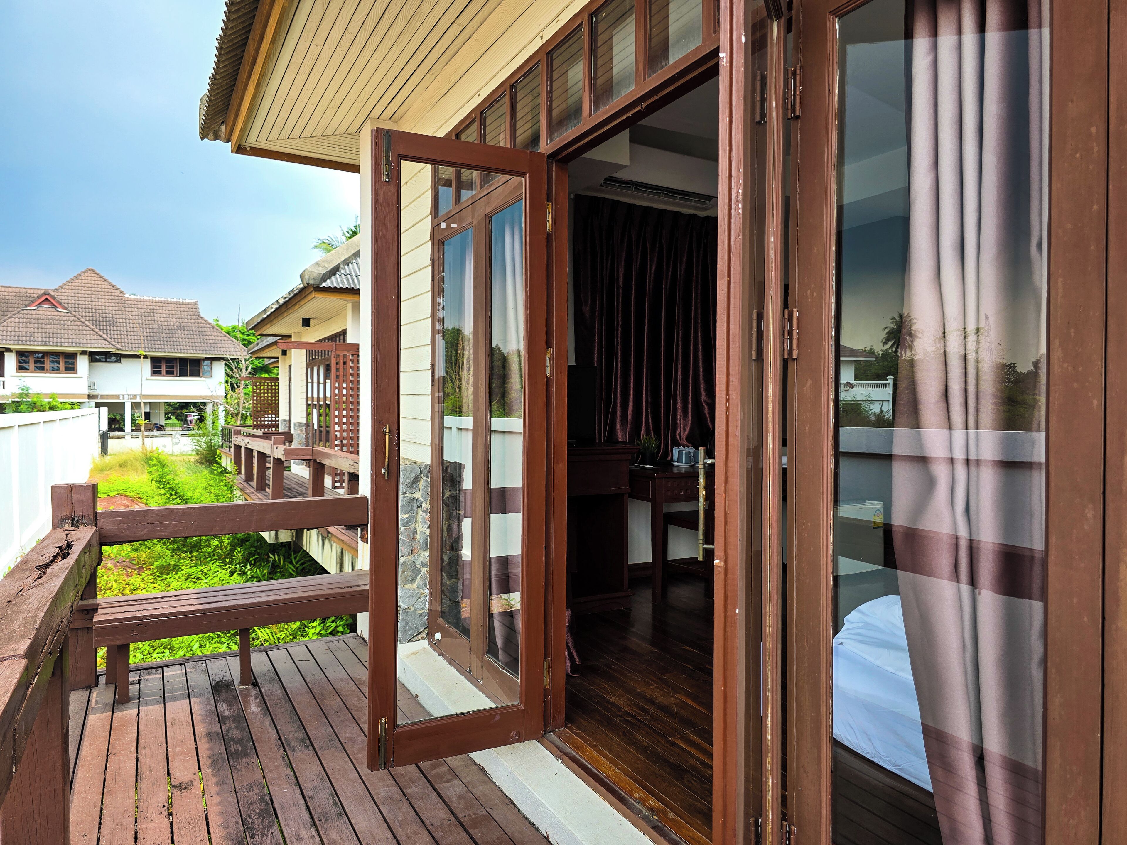 A wooden deck with a glass door leading to a room with a bed and a desk.