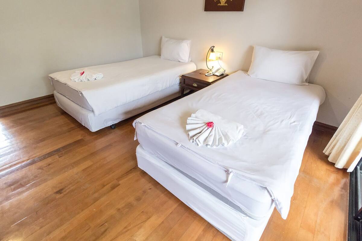 A hotel room with two single beds, a bedside table with a lamp, and a wooden floor.