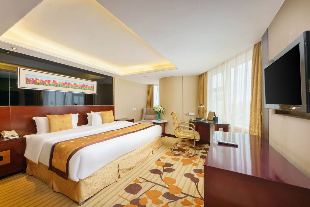 A hotel room with a large bed, a desk, a chair, a TV, and a painting on the wall.