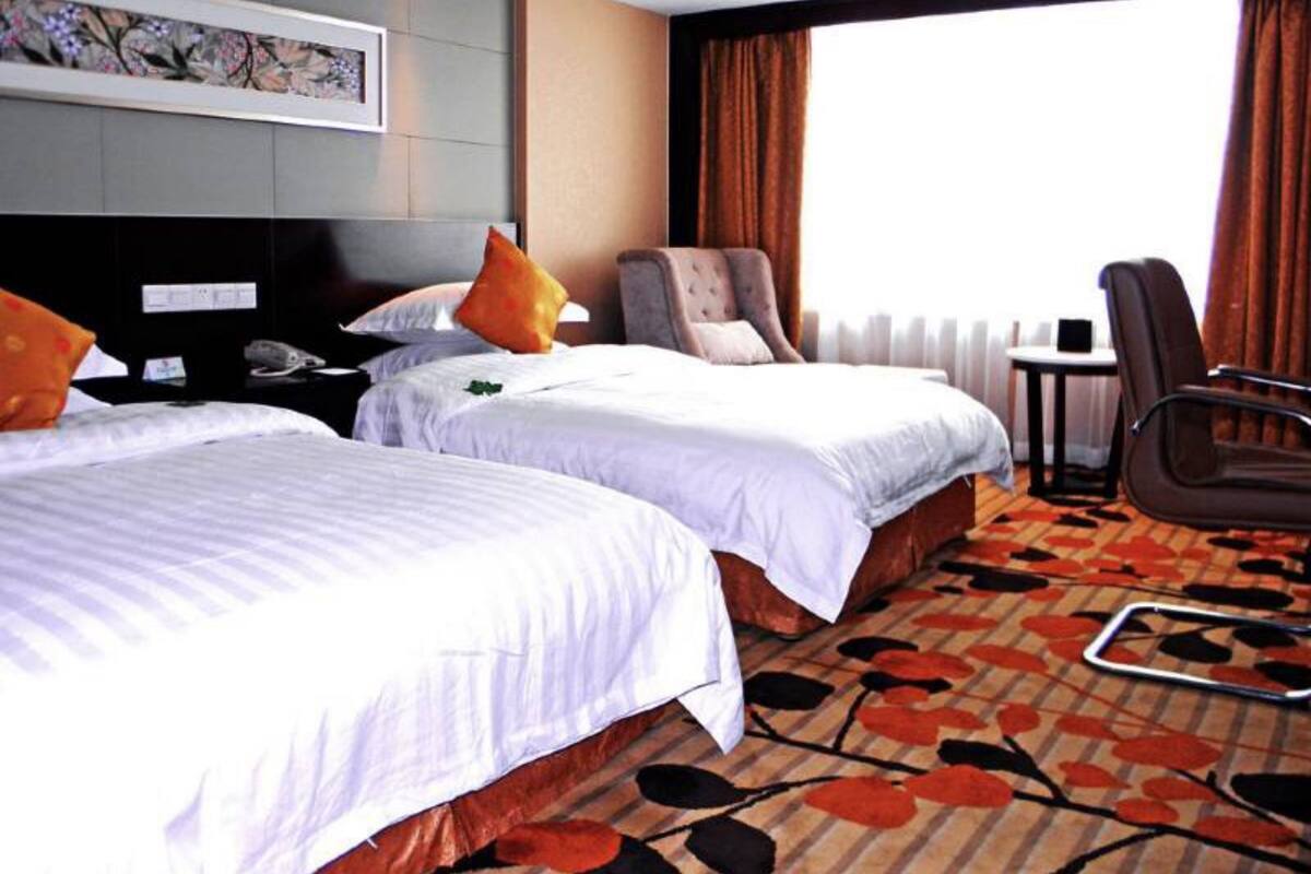 A hotel room with two beds, a desk, a chair, and a window with curtains.