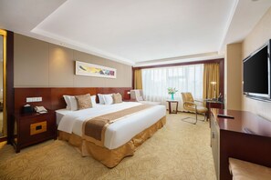 A hotel room with a large bed, a desk, a TV, and a window with curtains.
