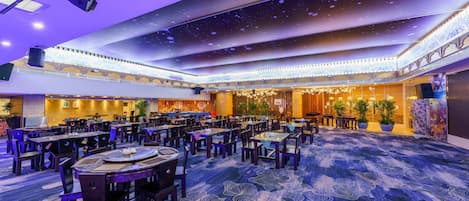 Un amplio salón de banquetes con múltiples mesas y sillas, un techo alto decorado con motivos que evocan estrellas, y una alfombra estampada.