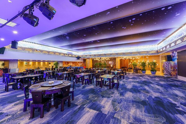 A spacious banquet hall with multiple tables and chairs, a high ceiling with star-like decorations, and a patterned carpet.