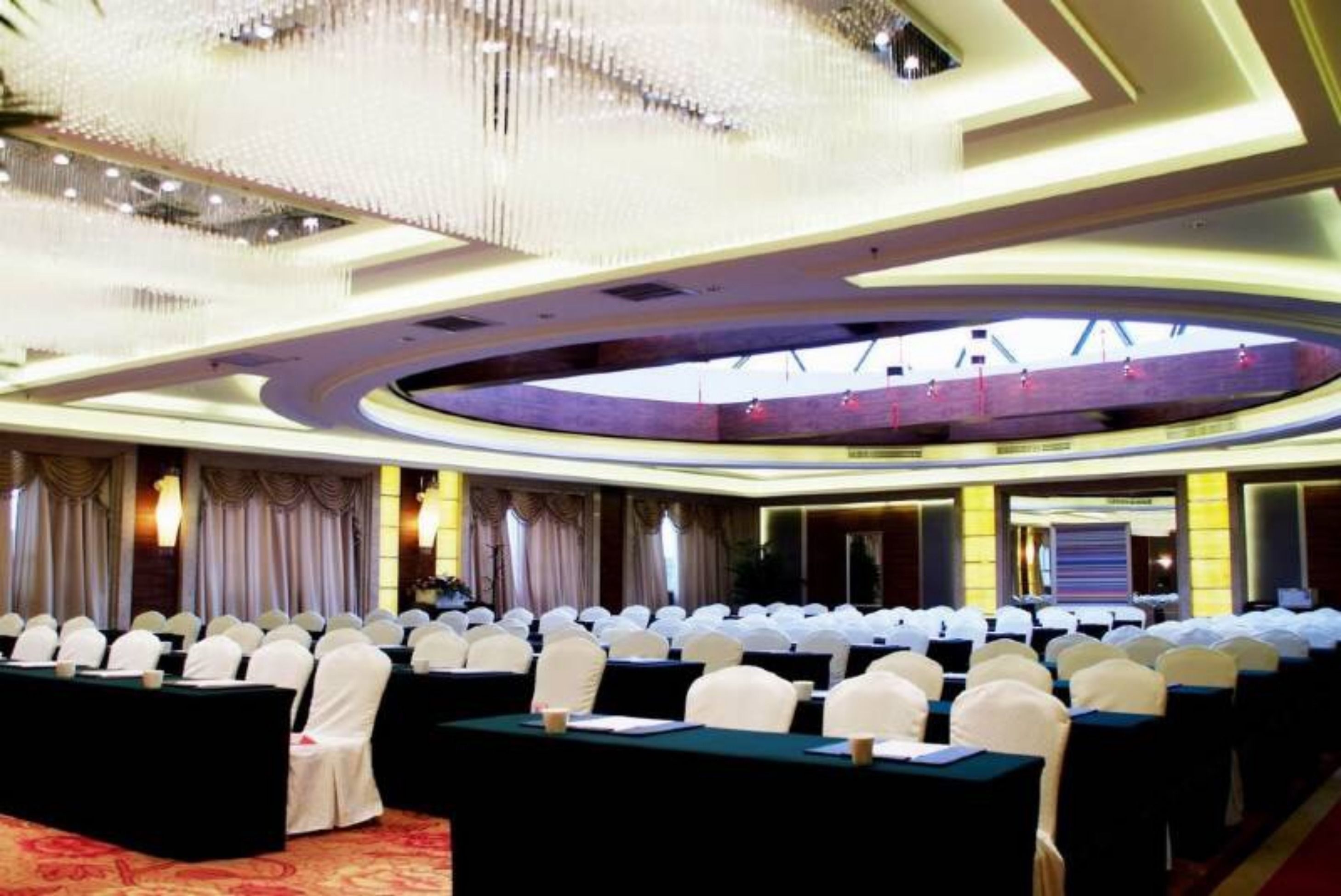 A conference room with rows of tables and chairs, a large chandelier, and a circular skylight.