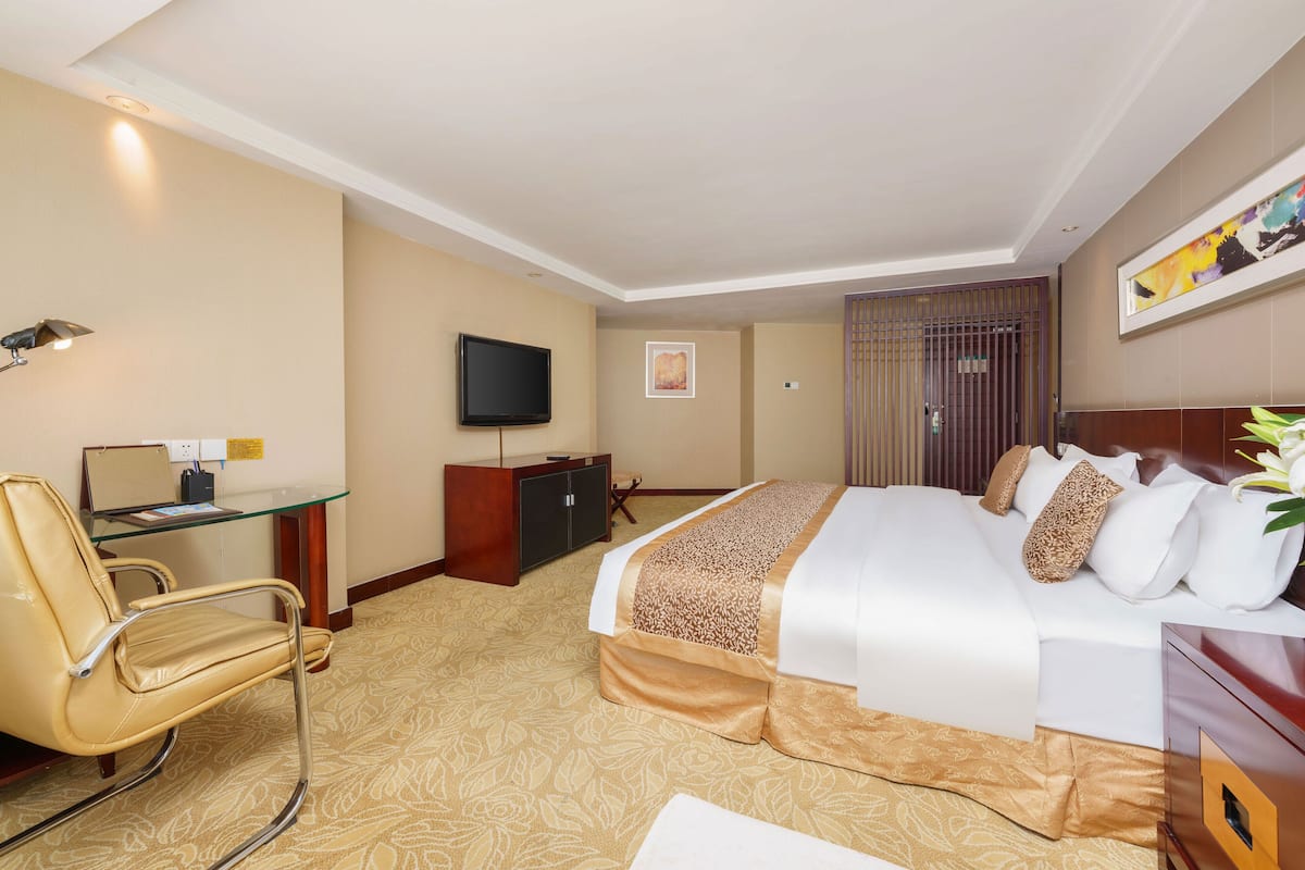 A hotel room with a bed, a desk with a computer, a TV, and a chair.