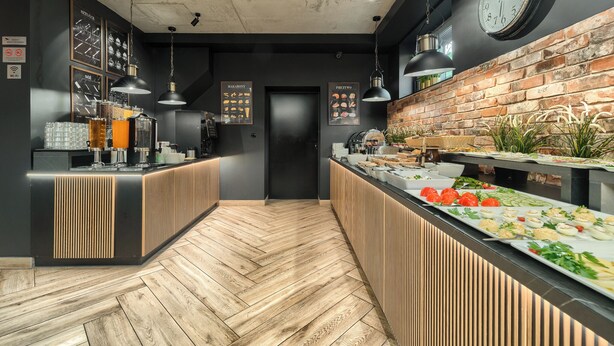 A modern kitchen with wooden flooring, a brick wall, and a buffet counter with various food items. - Stawa Villa & Apart (Swinoujscie)