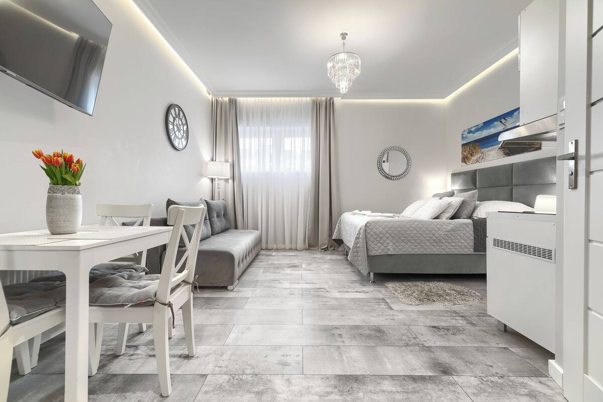 A modern, well-lit bedroom with a bed, bedside table, and a TV mounted on the wall.