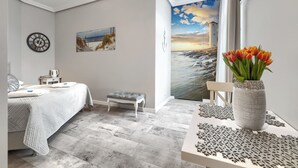 A bedroom with a bed, a bench, a clock, a painting, and a view of a lighthouse through a window. - Stawa Villa & Apart (Swinoujscie)