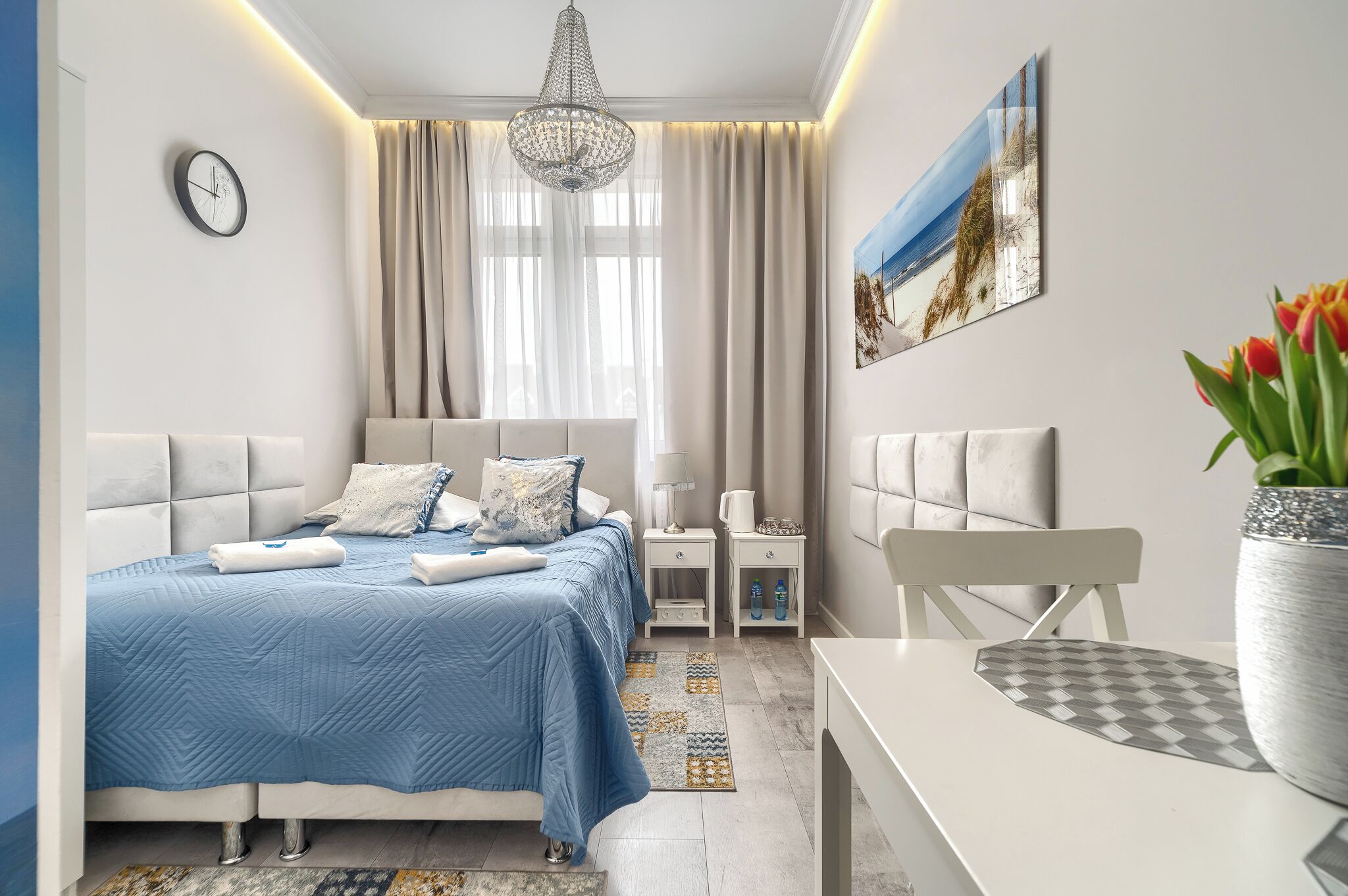 Een moderne slaapkamer met een bed, nachtkastjes, een stoel, een bureau en een groot raam met gordijnen.