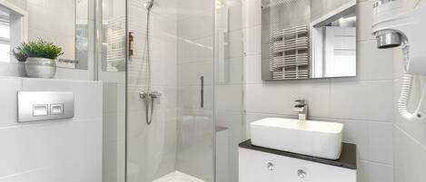 Un baño moderno con ducha acristalada, lavamanos blanco y tocador con cajones.