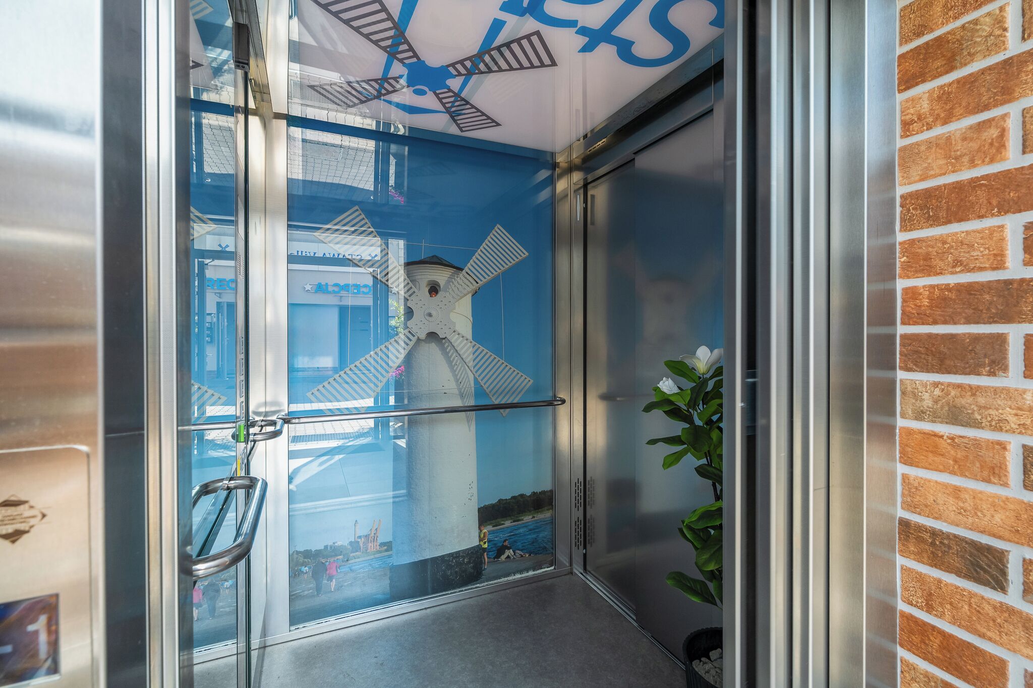 Une porte en verre avec une poignée en métal, un mur de briques et le reflet d’un moulin à vent.