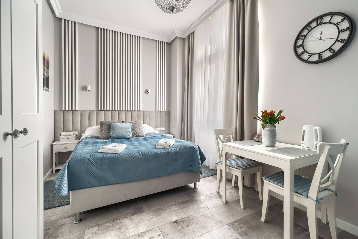 A modern hotel room with a bed, bedside table, and a dining area with a table and chairs.
