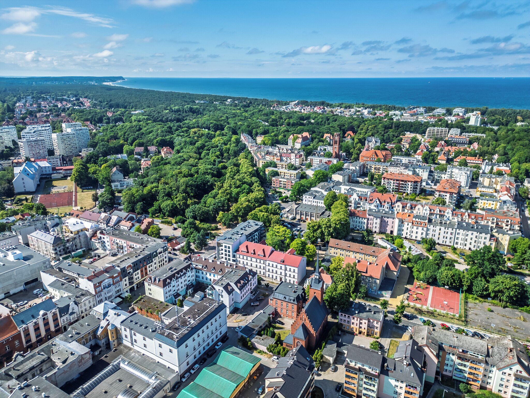 Luchtbeeld van een stad met dichte woongebouwen, een opvallende kerk en een kustlijn op de achtergrond.