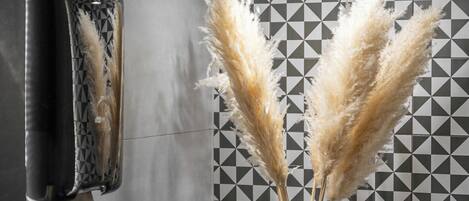A bathroom with a black and white checkered wall, a black and gold vase with pampas grass, and a hand dryer.