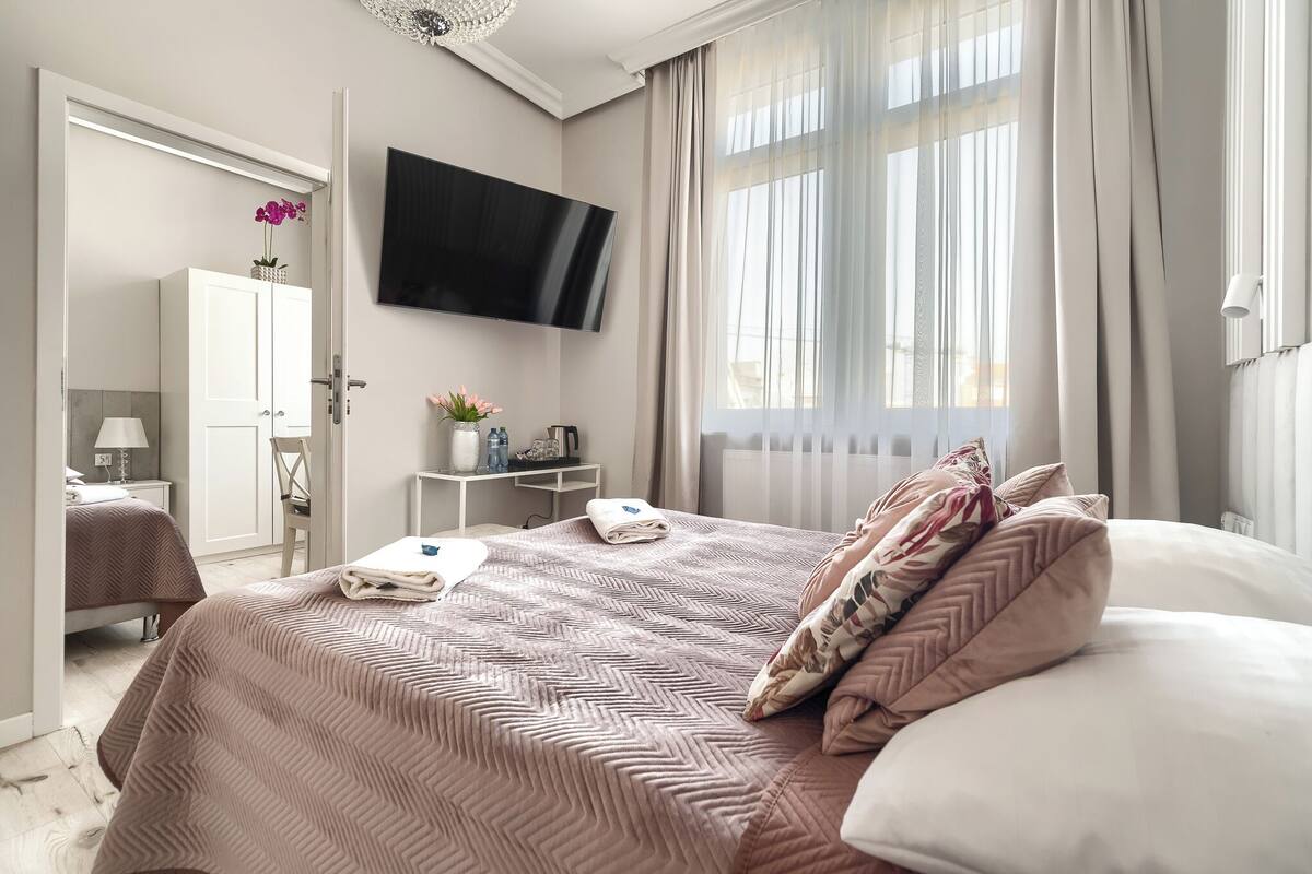 A modern hotel room with a large bed, a flat-screen TV, a desk with a lamp, and a wardrobe.