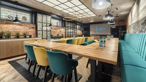 A modern dining area with a long wooden table, yellow and teal chairs, and a teal sofa. - Stawa Villa & Apart (Swinoujscie)