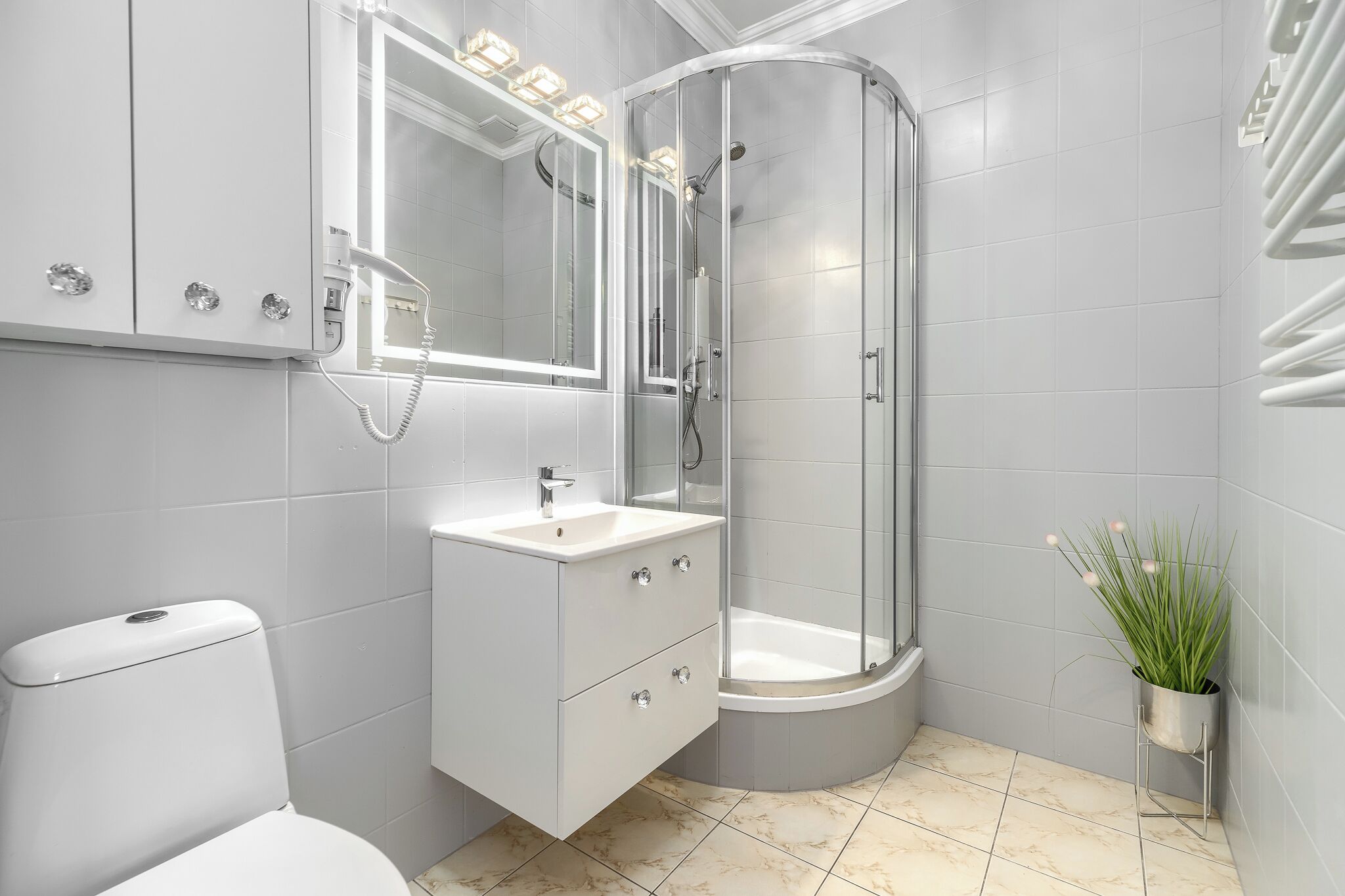 Un baño moderno con inodoro, tocador, lavamanos, espejo, ducha y una planta en maceta.