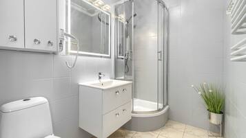 A modern bathroom with a toilet, vanity, sink, mirror, shower, and a potted plant.