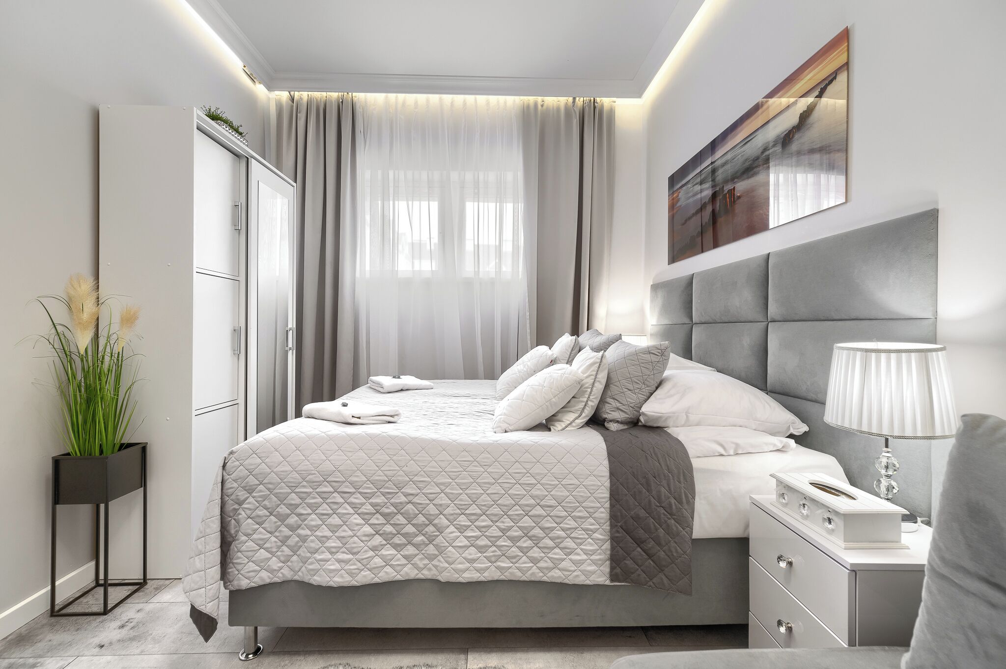 A modern bedroom with a bed, bedside table, lamp, and a painting on the wall.