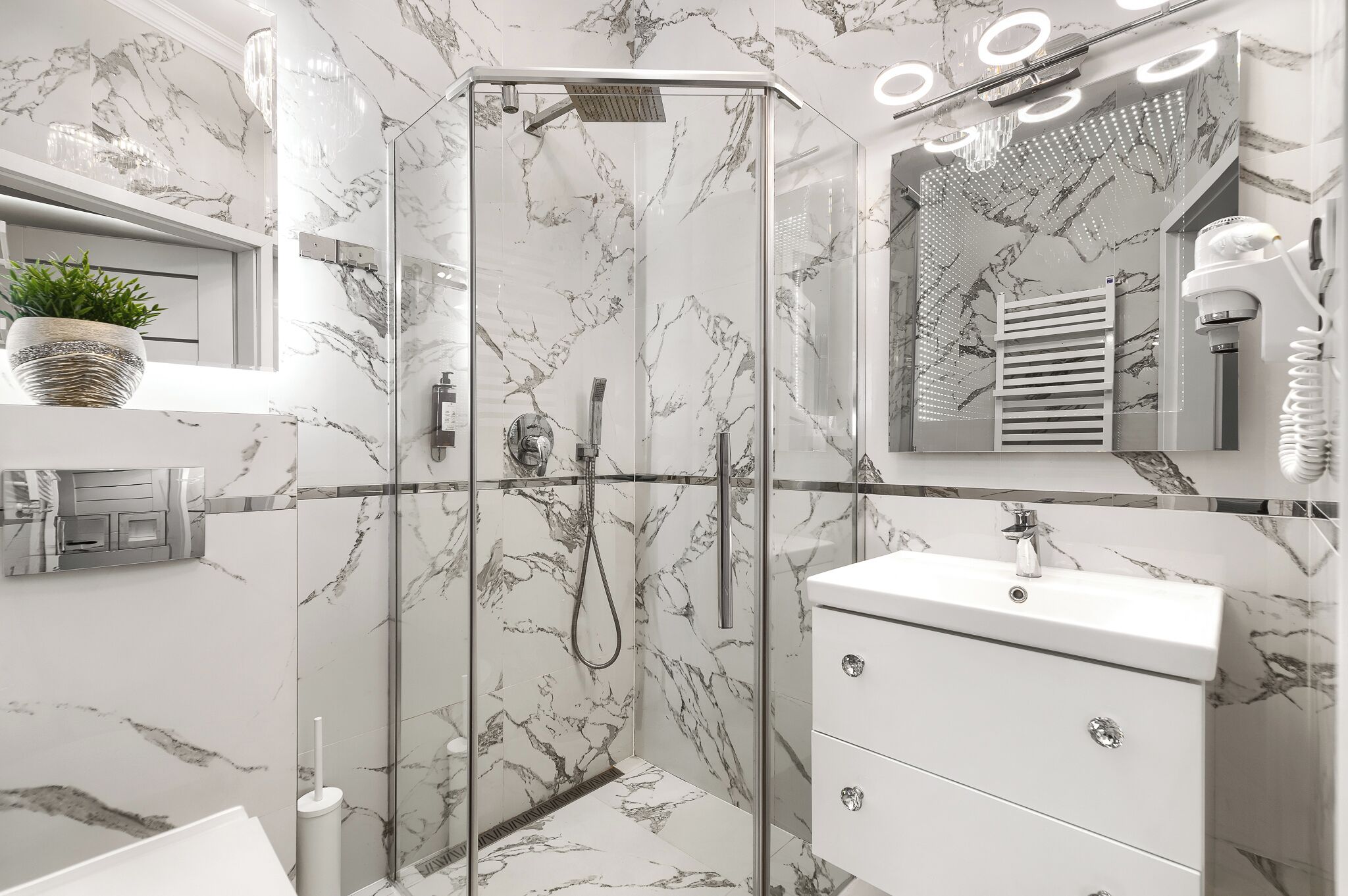 A modern bathroom with a glass-enclosed shower, marble walls, a white sink, and a mirror with built-in lighting.