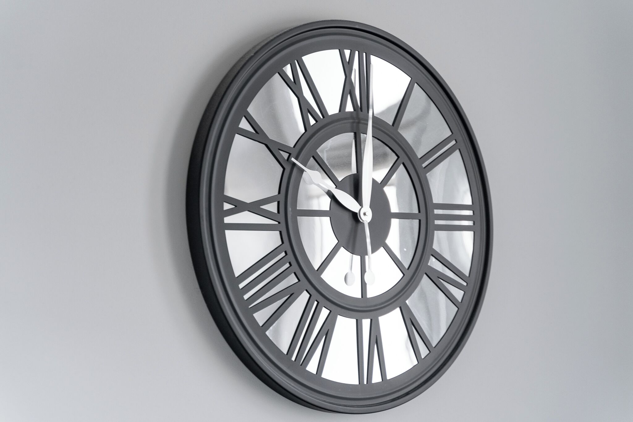A wall-mounted clock with a minimalist design, featuring Roman numerals and a sleek, modern aesthetic.
