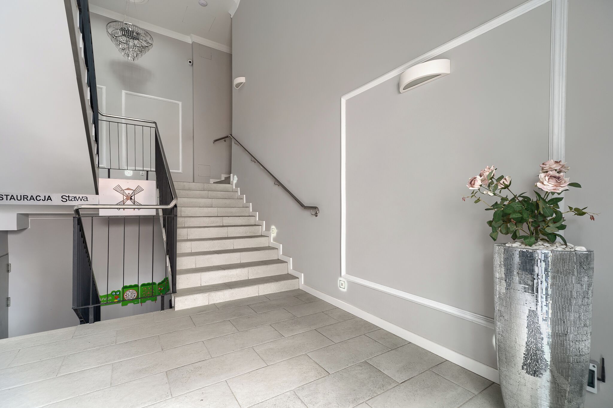 A staircase with a handrail, a wall-mounted light, and a potted plant with flowers.