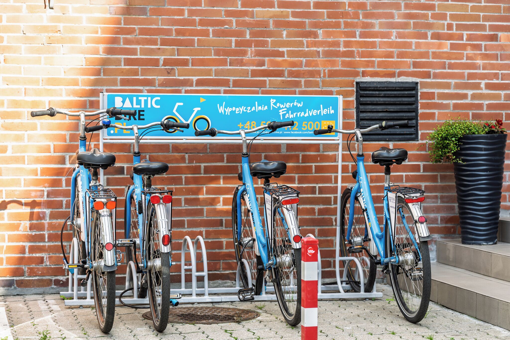 A row of bicycles parked against a brick wall with a sign above them.