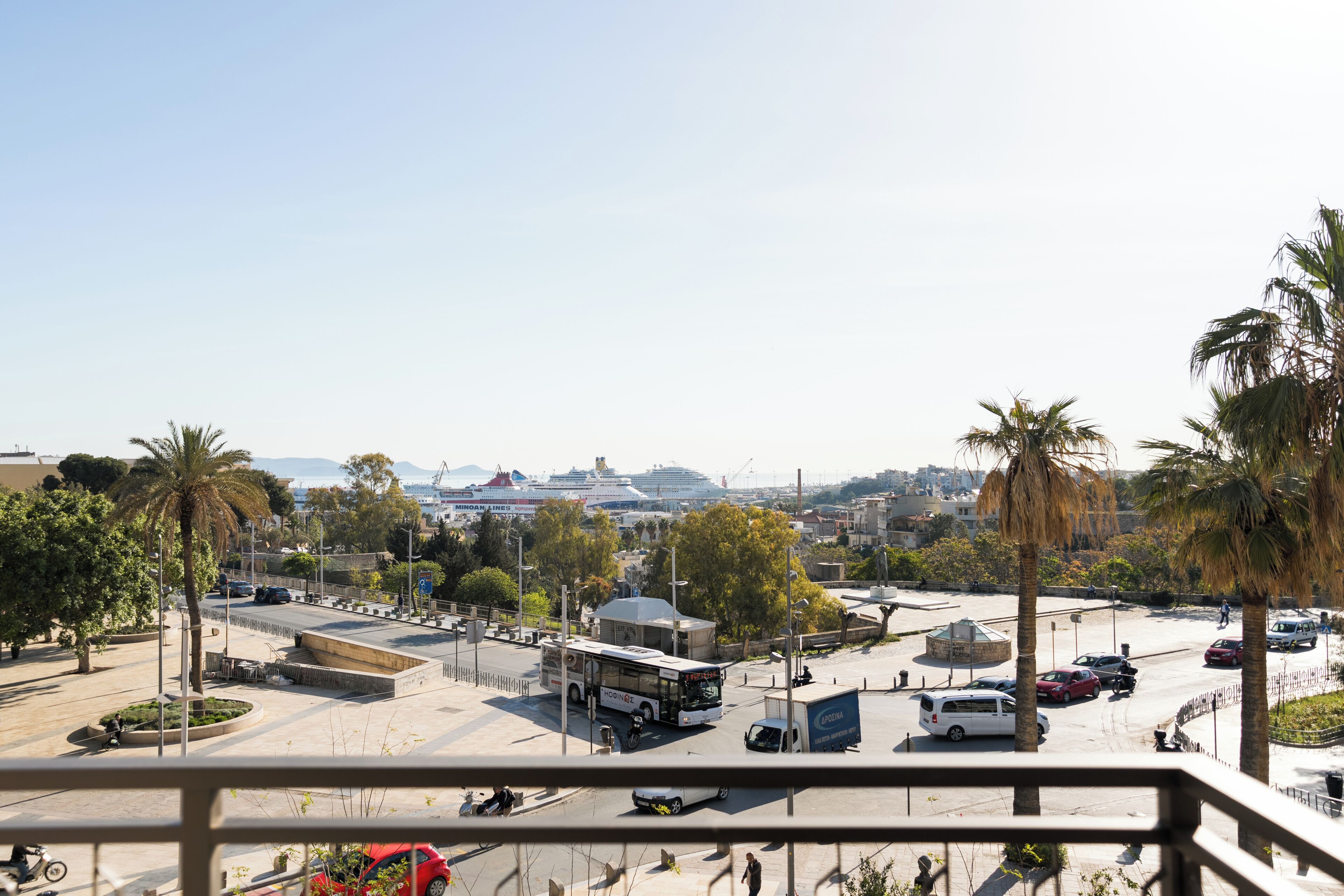 Vista de un paisaje urbano con un autobús, automóviles y palmeras.