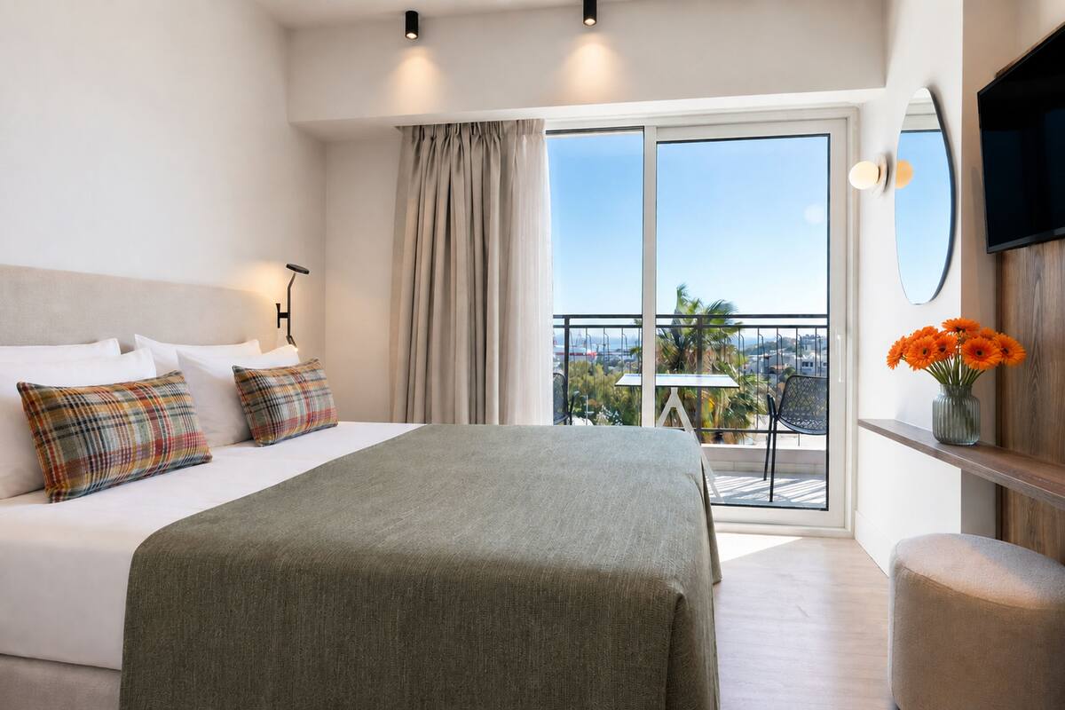 Une chambre d’hôtel avec un lit, un balcon offrant une vue, une télévision et un vase rempli de fleurs.