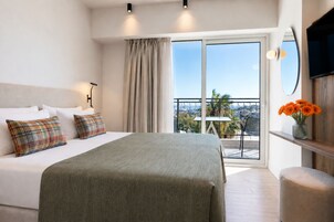 Quarto de hotel com cama, varanda e vista, televisão e um vaso com flores.