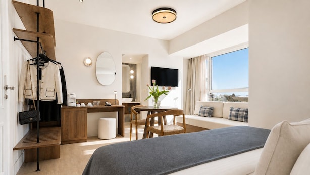 Una camera d'albergo moderna con un letto, una scrivania, una sedia, un tavolino con un vaso di fiori, uno specchio e un'ampia finestra.