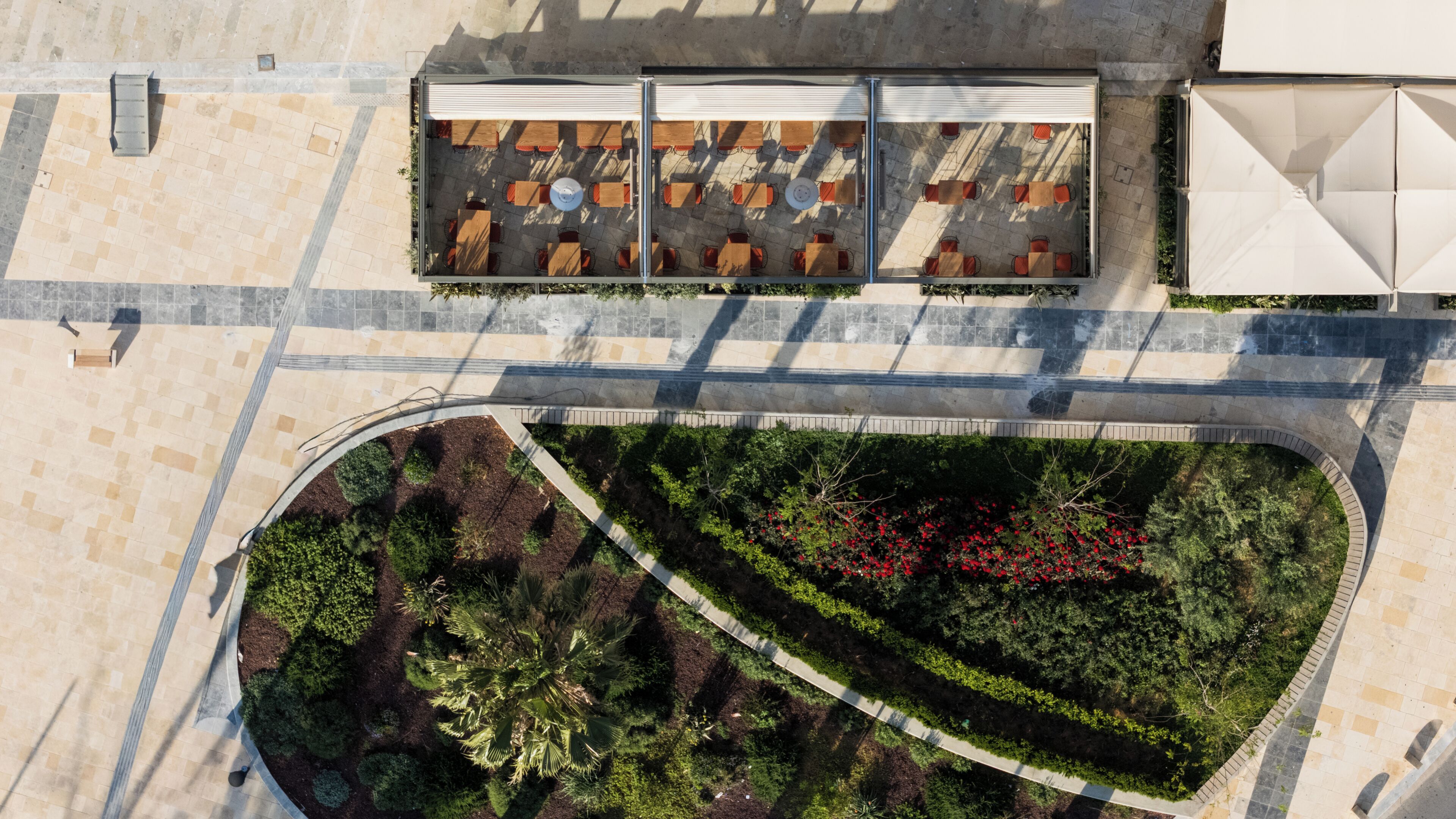 Vue aérienne d’un jardin aménagé sur un toit, avec des espaces de détente, un chemin et les bâtiments environnants.