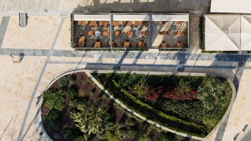 Vista aérea de um jardim no terraço com áreas de estar, um caminho e edifícios ao redor.