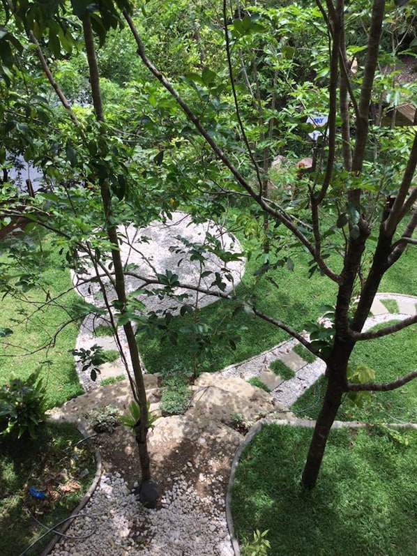 Un jardin avec un sentier en pierre, des arbres et une grande formation rocheuse.
