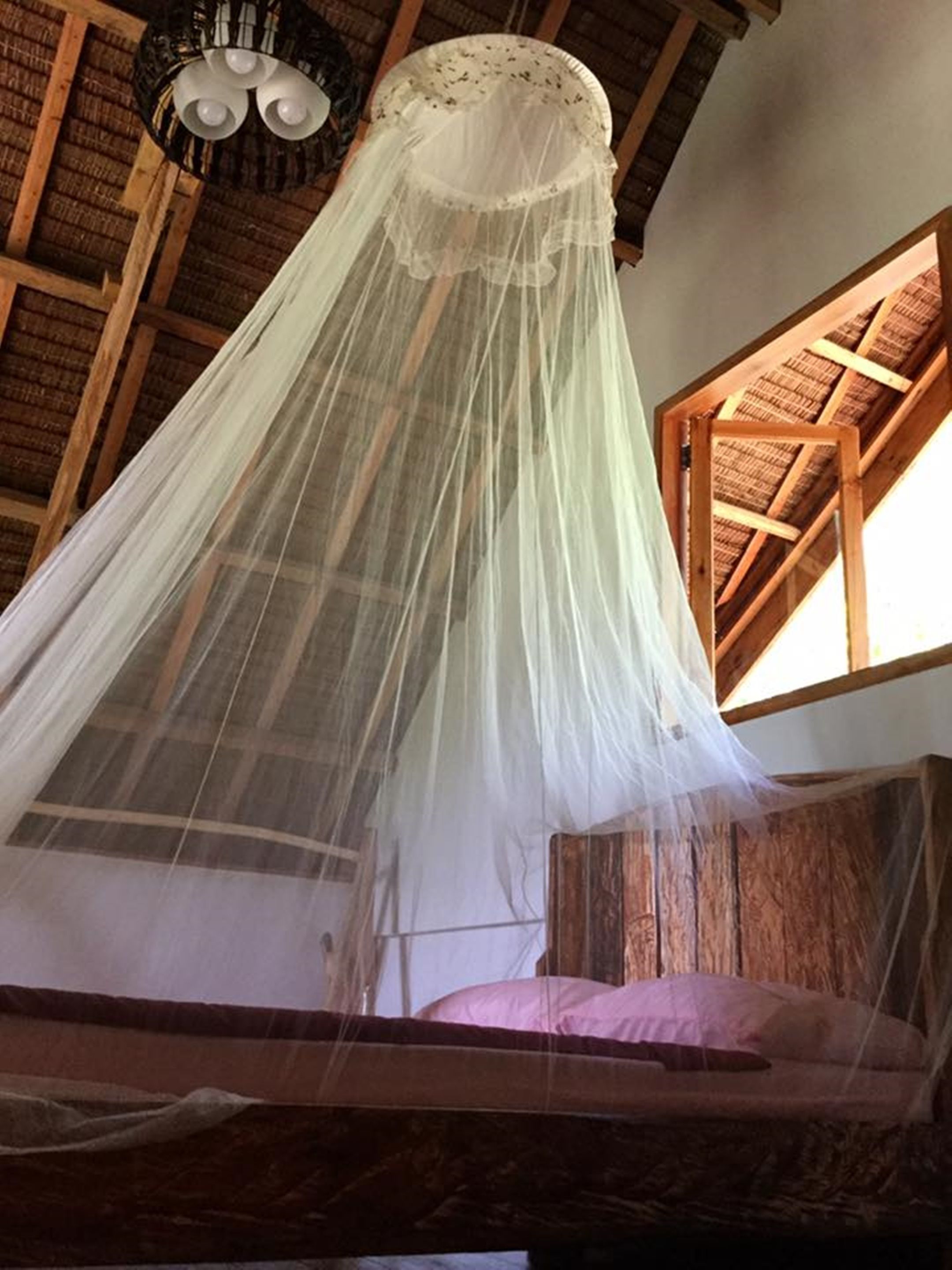 A bed with a white canopy, wooden beams, and a window with a wooden frame.